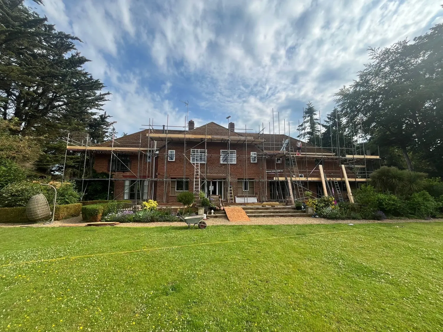 Large renovation scaffold viewed across landscaped gardens beneath a dramatic sky