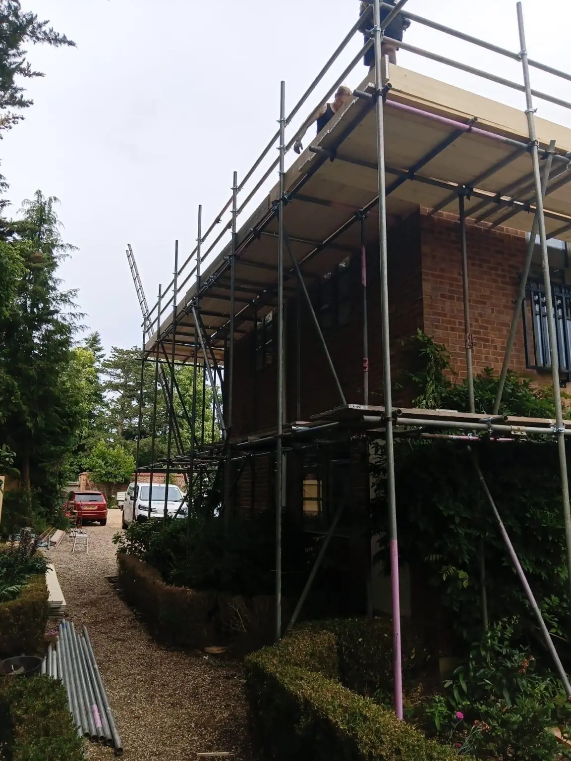Multi-lift scaffold fitted along a restricted side passage beside established hedging